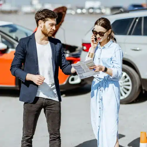 Man and woman looking ovr paperwork with a car accident in the background - car accident law firm in Kennesaw, GA