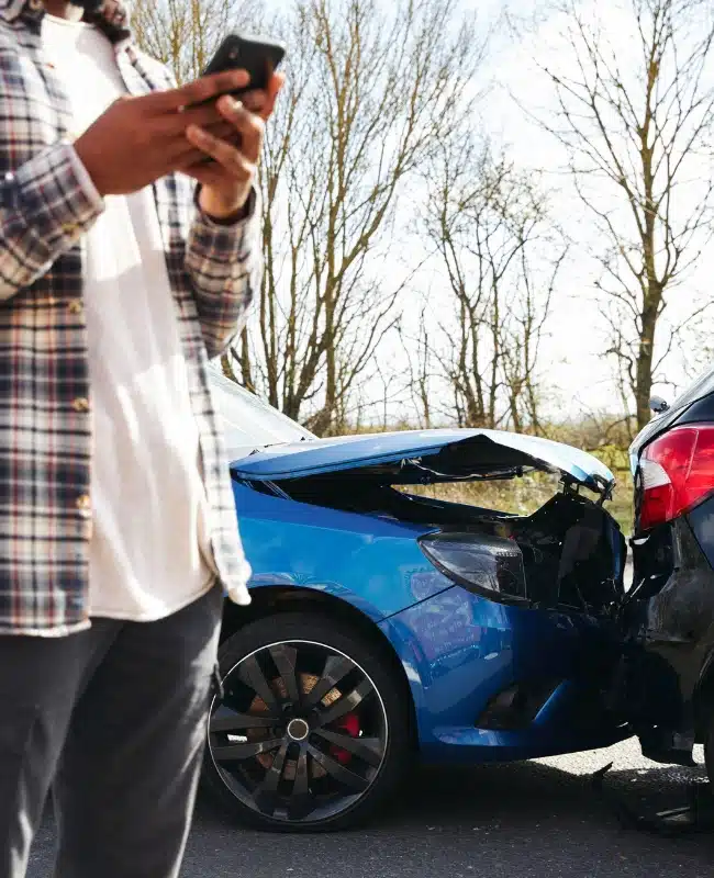Car accident in background with man in foreground using a phone - Car Accident Lawyers In Kennesaw Georgia